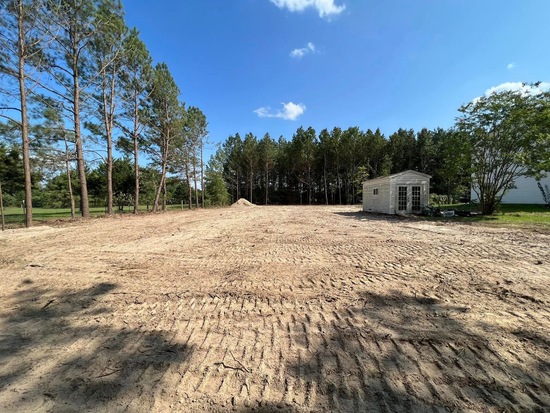 A dirt field with a house in the background and trees in the background.