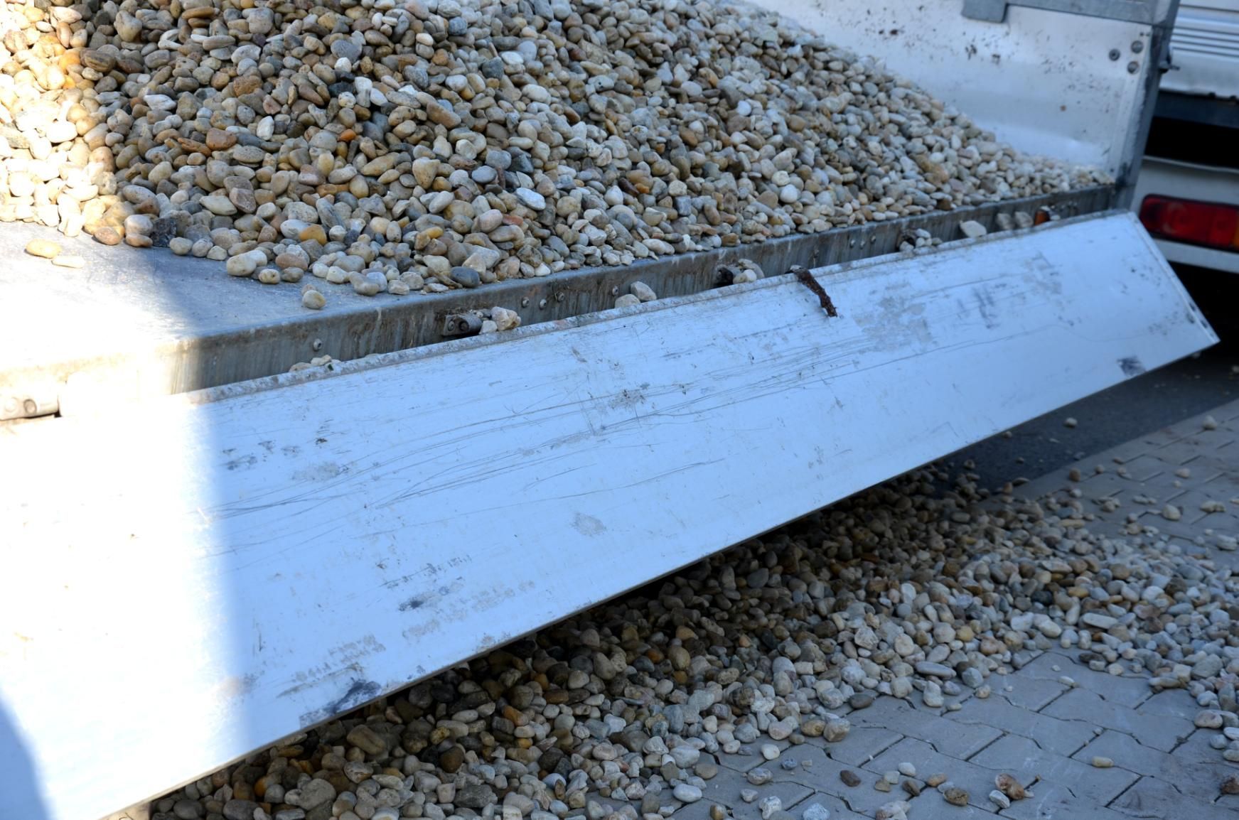 White metal skid plate covering a gravel-filled trench beside a paved surface outdoors