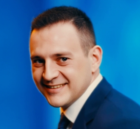 Ein Mann in Anzug und Krawatte lächelt vor einem blauen Hintergrund