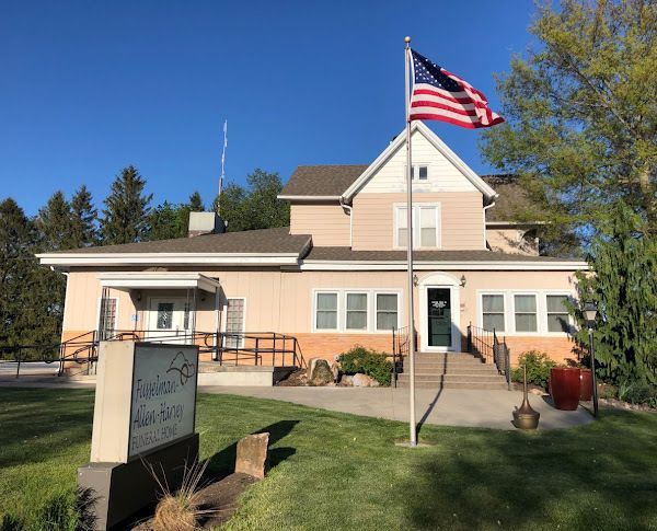 A two-story tan building with a porch, American flag, and a sign.