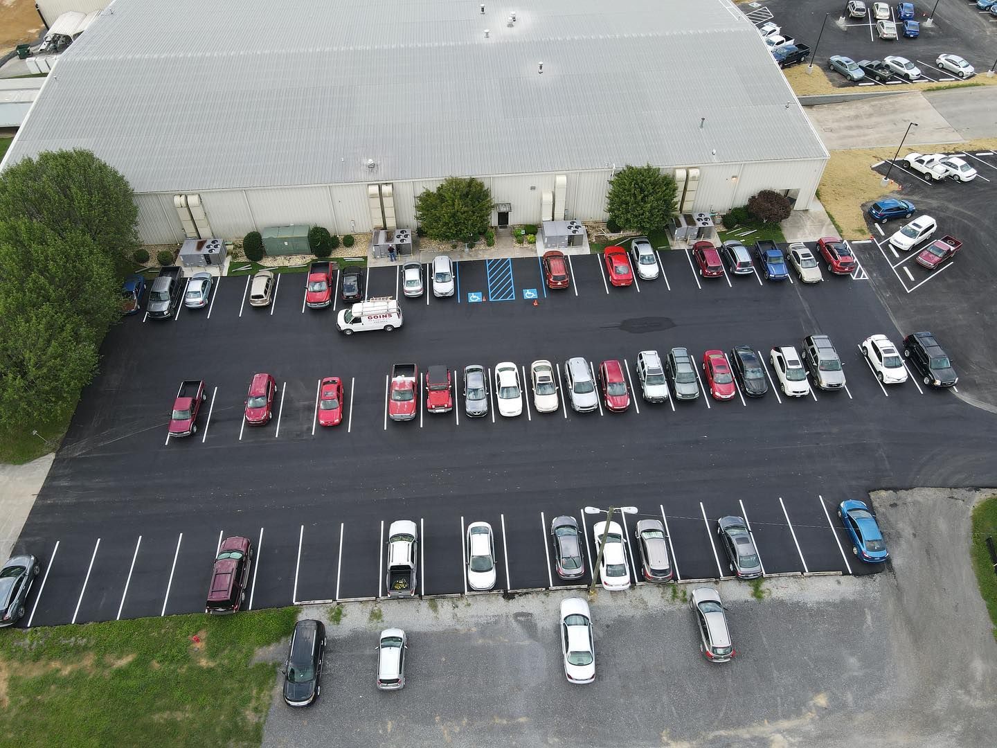 A row of cars are parked in a parking lot in front of a building.