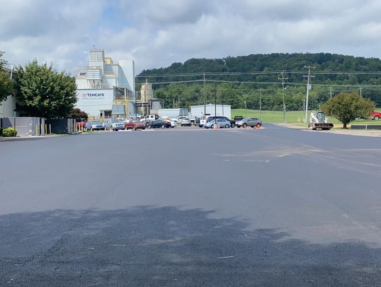 A lot of cars are parked in a parking lot in front of a factory.