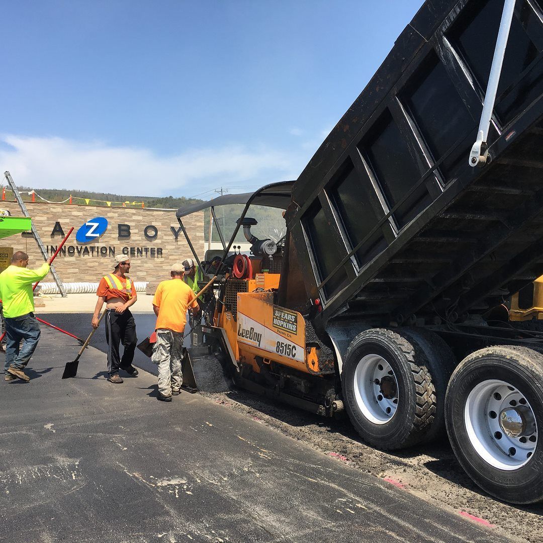 A group of construction workers are standing around a dump truck that is being loaded with asphalt