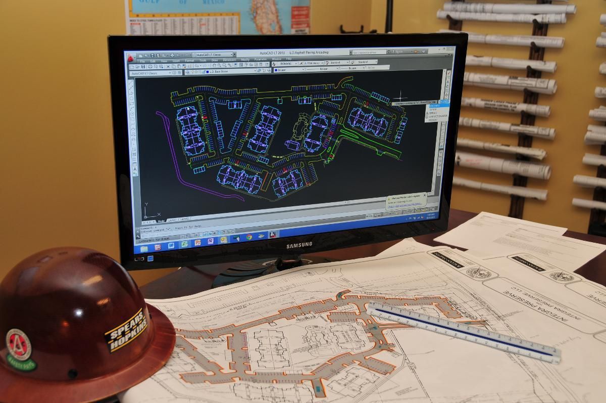 A hard hat sits on a desk next to a computer monitor