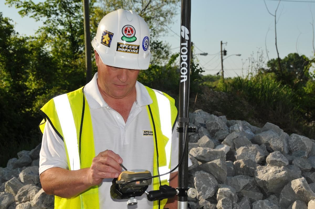 A man wearing a hard hat and safety vest is using a topcon device