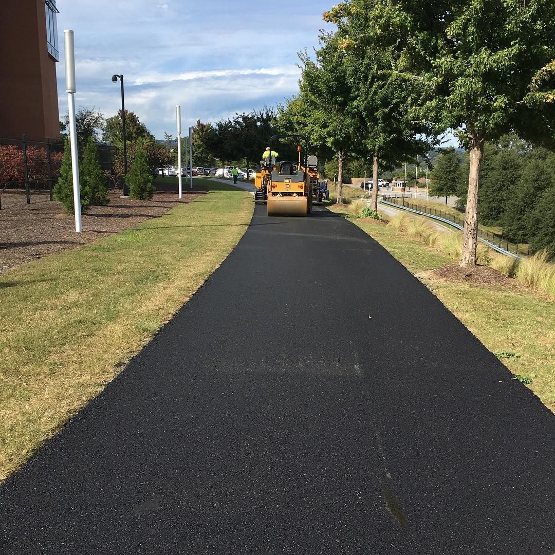 A yellow tractor is driving down a black road.