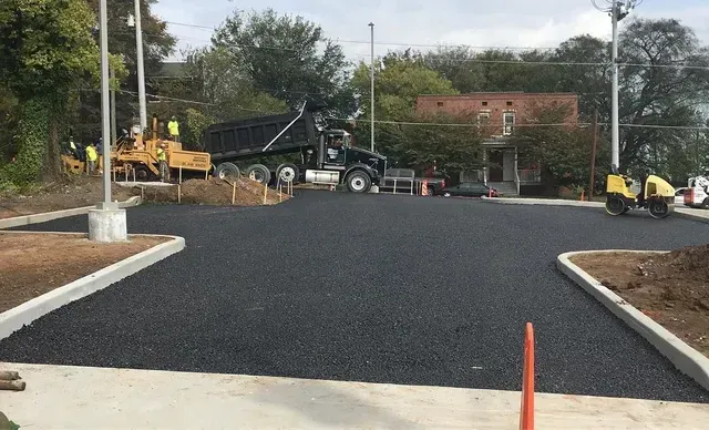 A dump truck is being loaded with asphalt in a parking lot.