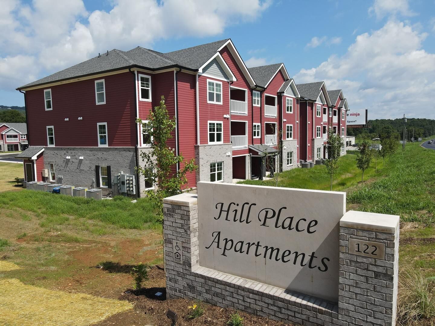 A sign for hill place apartments is in front of a red building