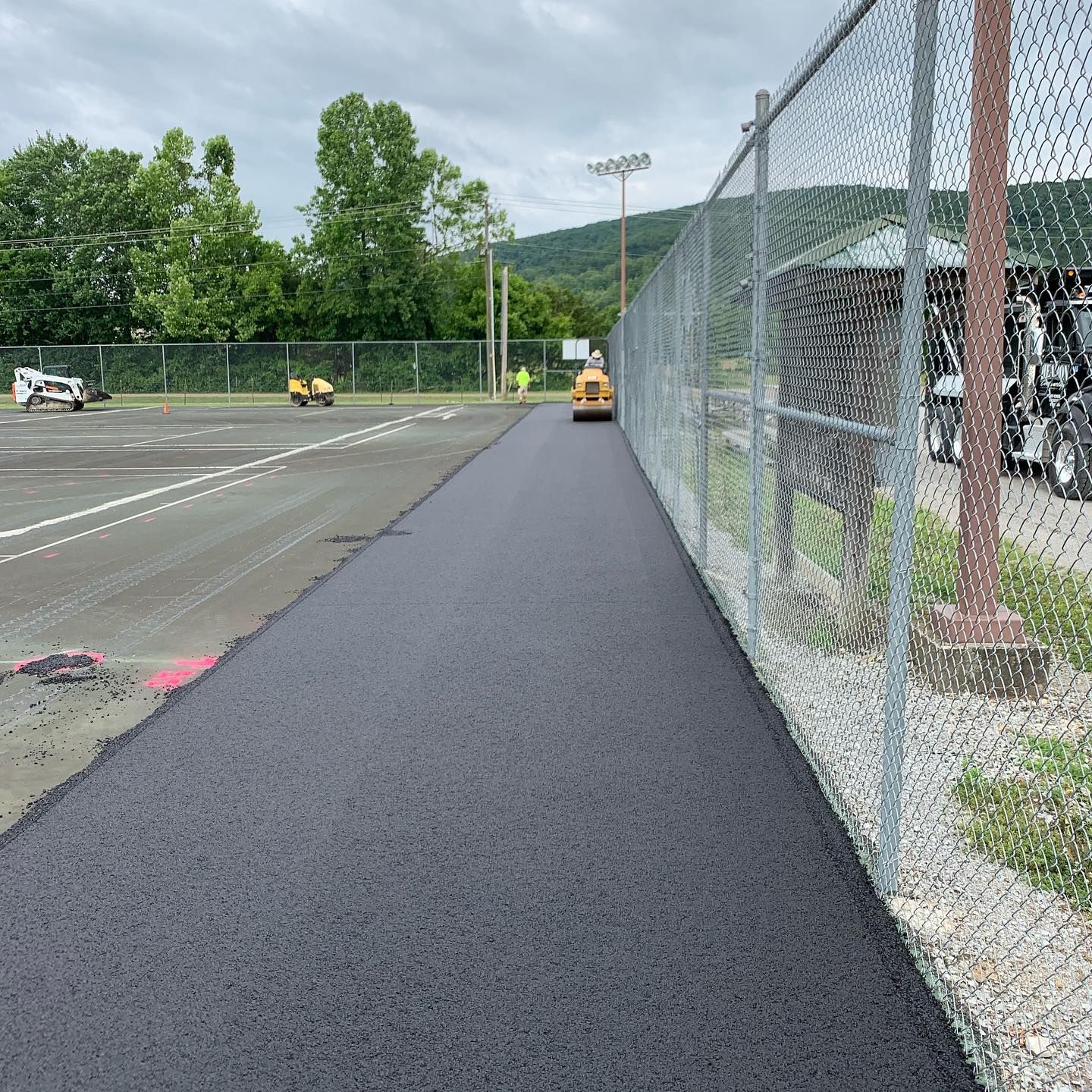 A chain link fence surrounds a road that is being paved