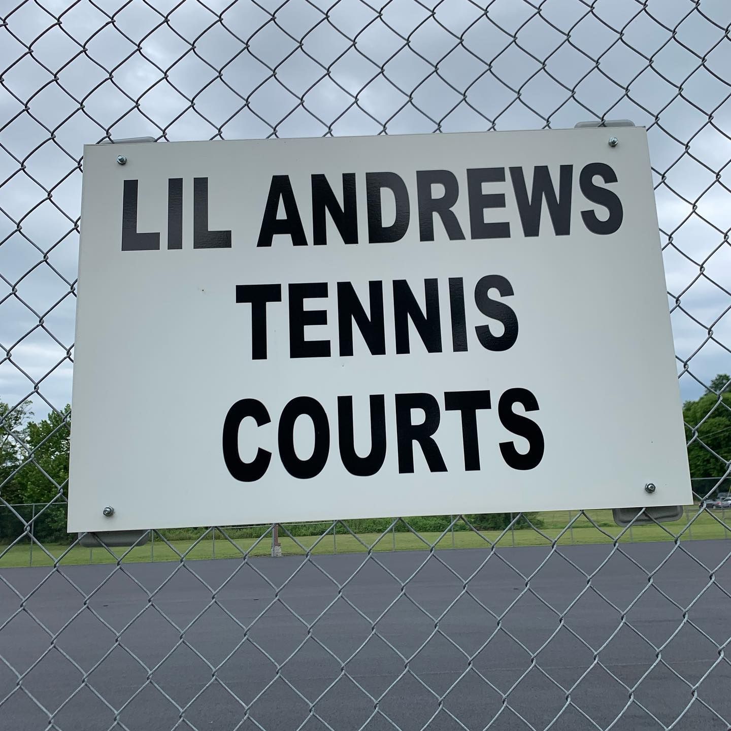 A sign on a chain link fence says lil andrews tennis courts