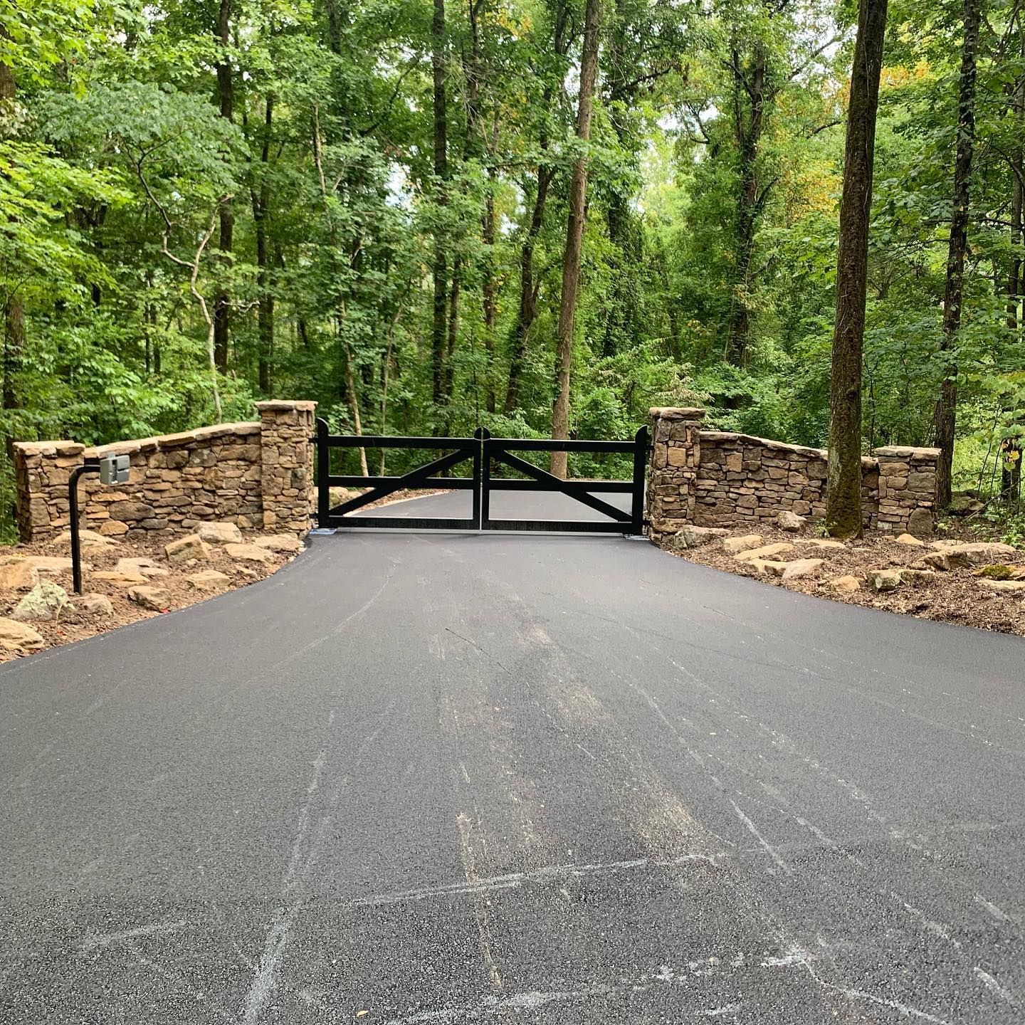 A driveway with a stone wall and a black gate