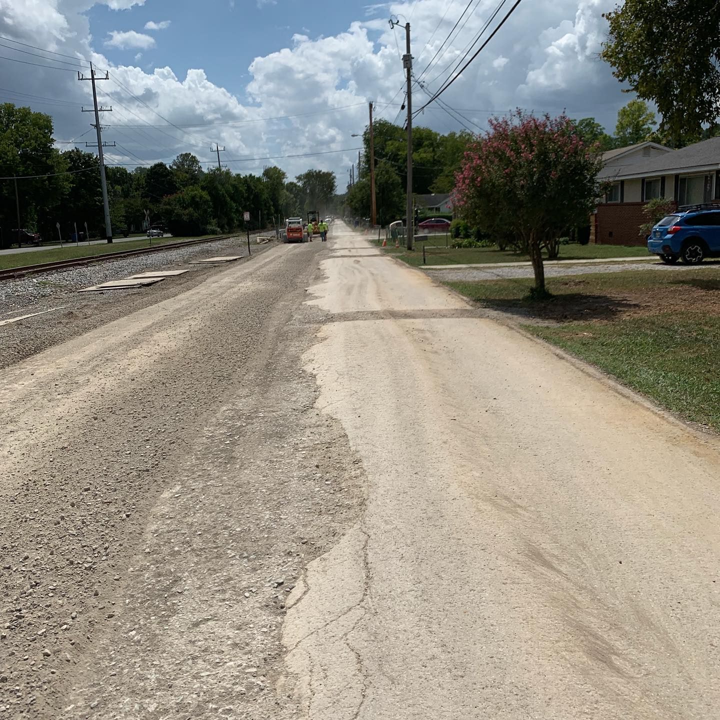 A dirt road with a blue car parked on the side of it