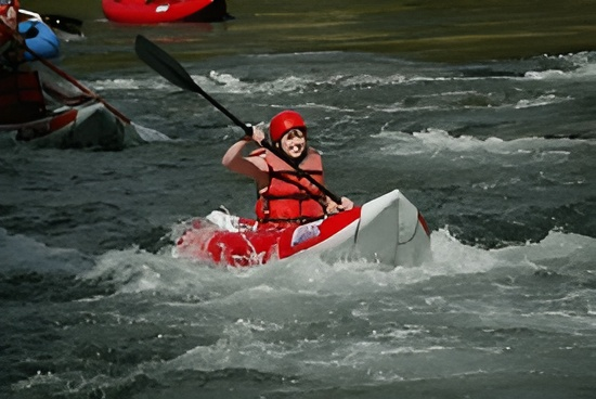 A man in a red helmet is paddling a white kayak