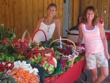 Two women are standing in front of a table filled with fruits and vegetables.