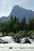 A group of people are rafting down a river with a mountain in the background.