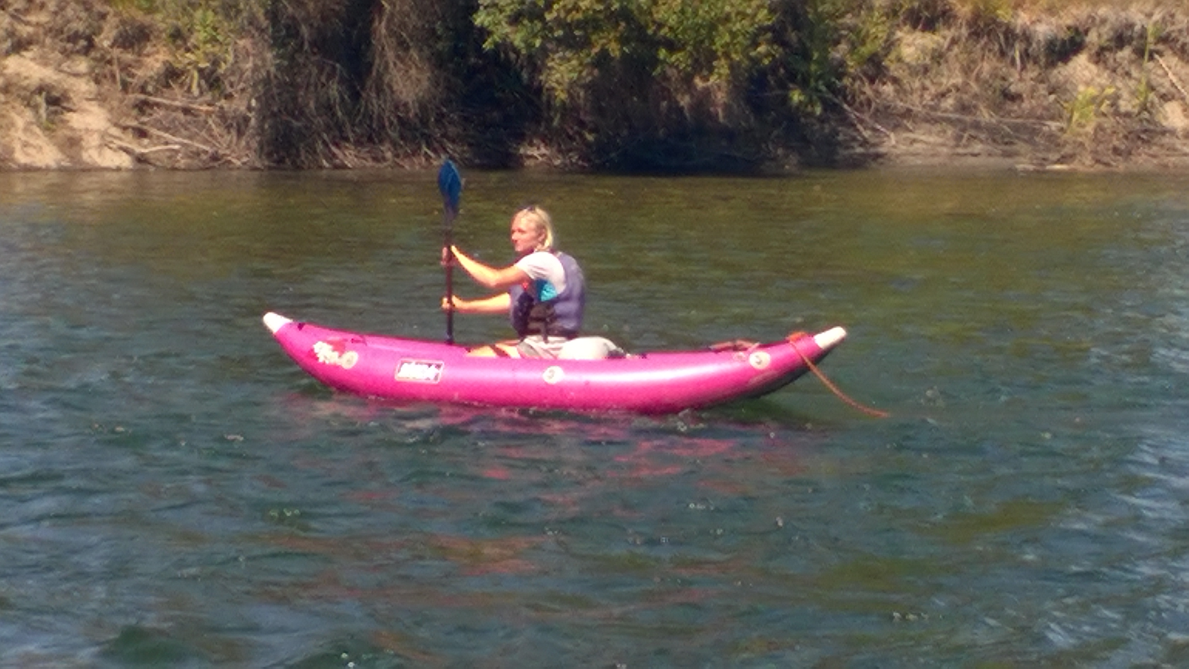 A man wearing a helmet and sunglasses is paddling a kayak