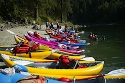A row of kayaks are lined up on the shore of a lake.