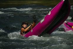 A woman in a pink kayak is going down a river.