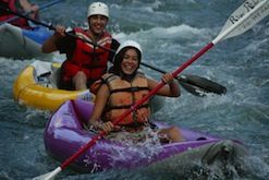 A man and a woman are rowing rafts down a river.
