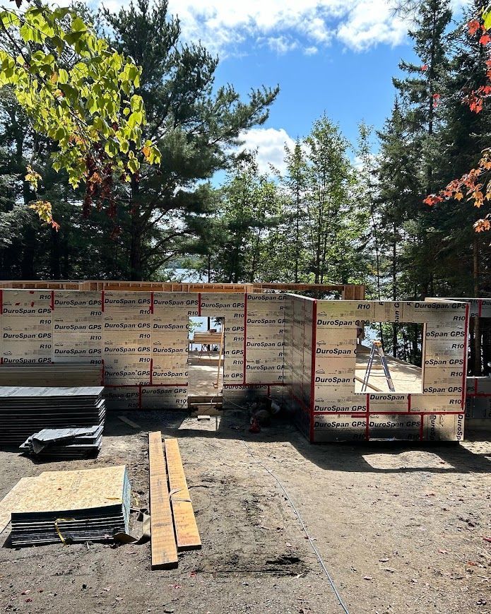 Construction site, partially built wall with insulation, windows, and lumber, trees in background.