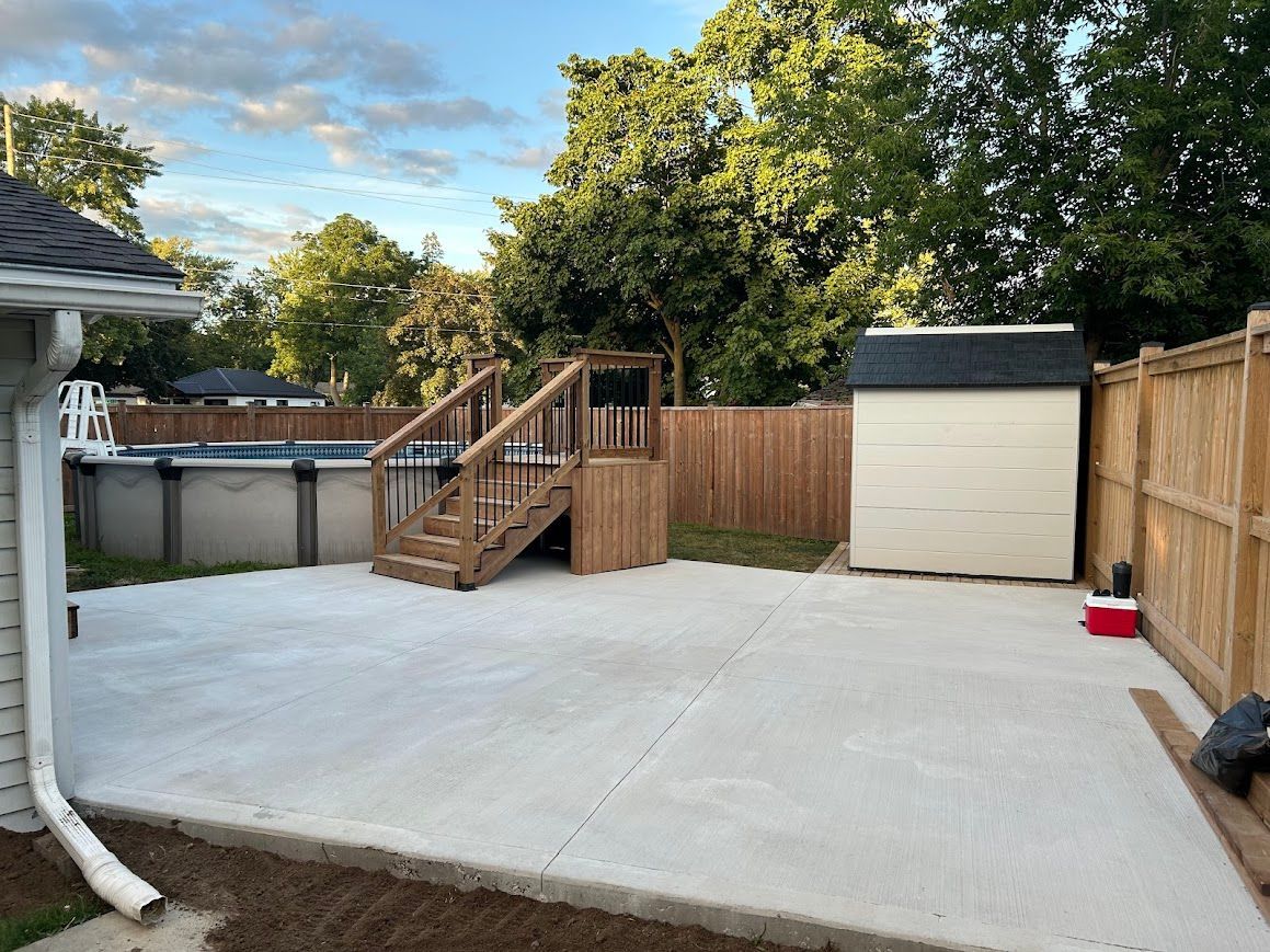 Backyard with concrete patio, above-ground pool, shed, wooden fence, and trees.