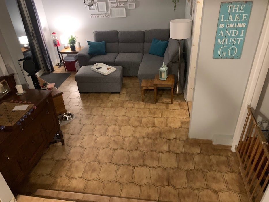 Living room with gray sectional, ottoman, lamp, and wall sign reading “The lake is my happy place”