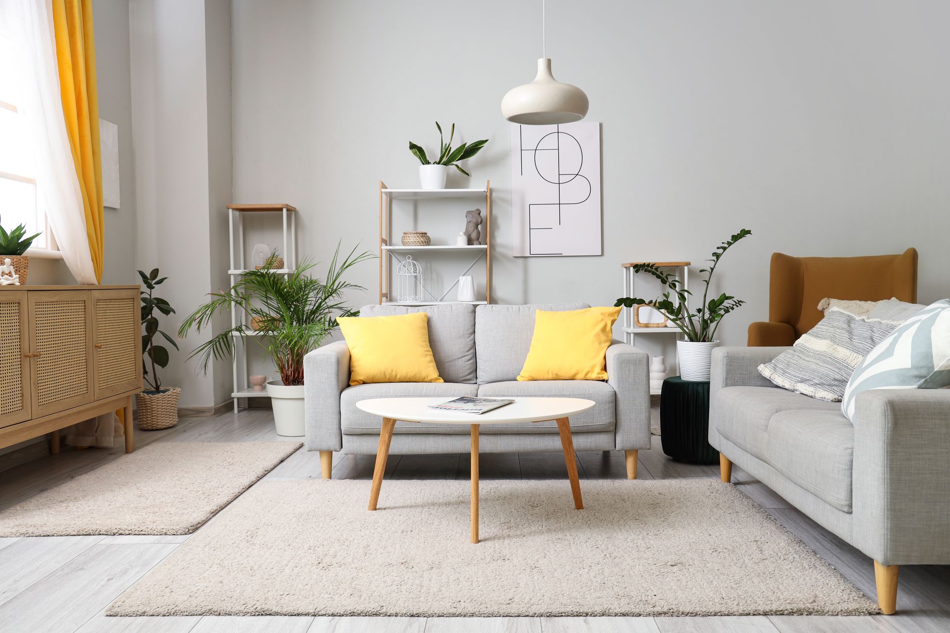 Living room with gray sofas, yellow pillows, plants, wooden furniture, and a rug.