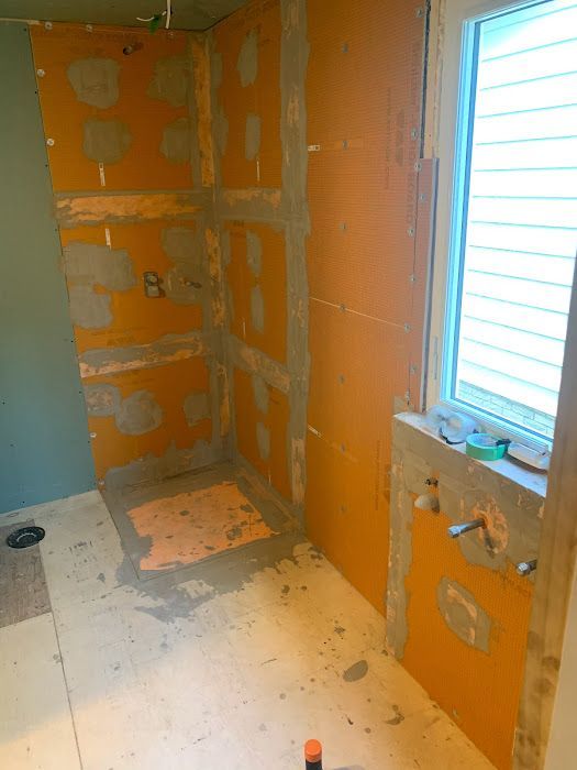 Shower stall under construction, orange waterproofing panels installed. Gray mortar visible, window present.