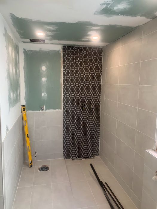 Bathroom renovation with tiled walls, partial black mosaic wall, and exposed drywall.
