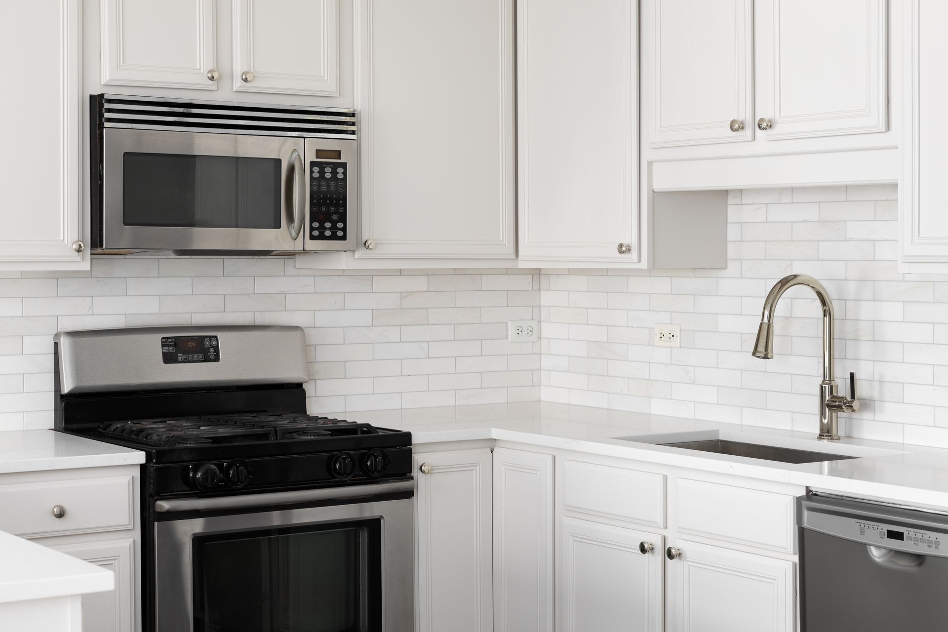 White kitchen with stainless steel appliances, white cabinets, and white subway tile backsplash.