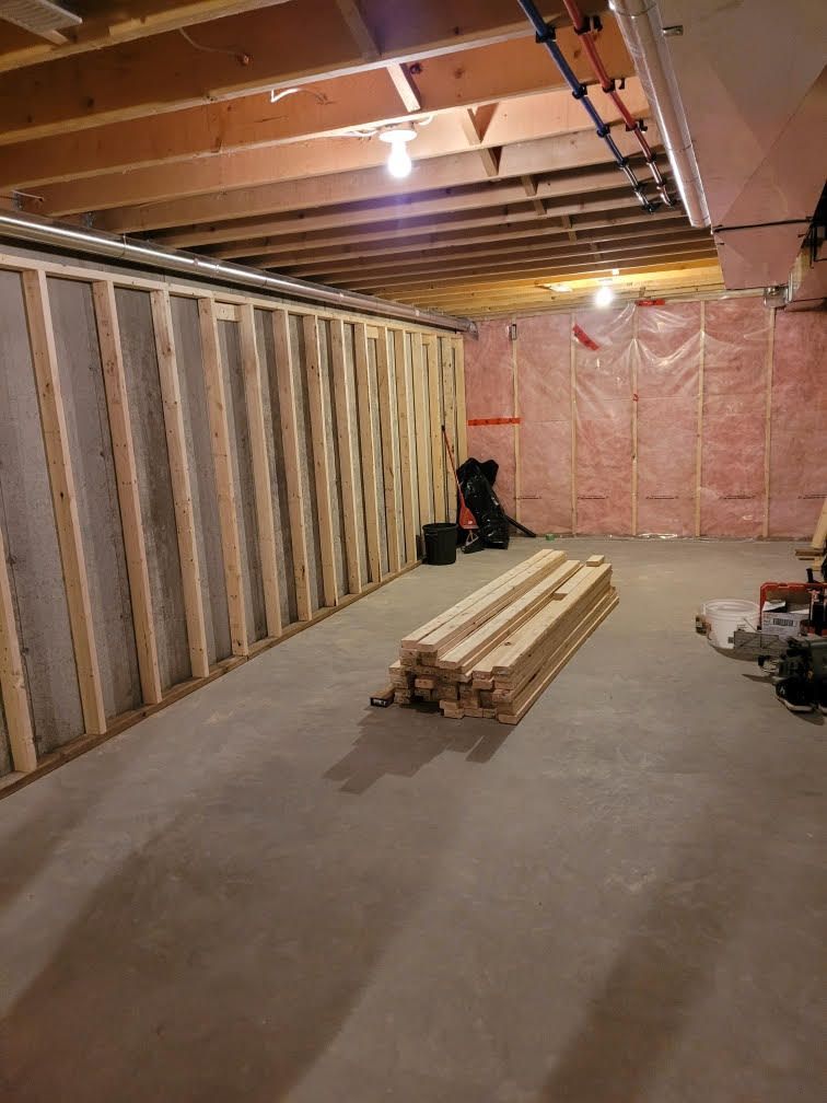 Unfinished basement with wooden framing, insulation, concrete floor, and lumber stack.