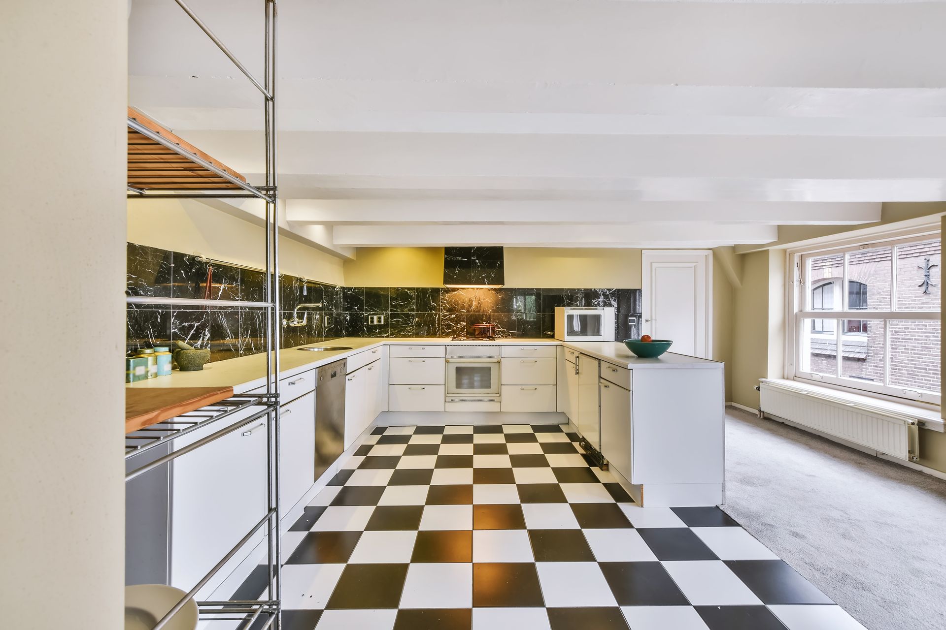 Black and white checkered floor in a white kitchen with stainless steel appliances and a window.