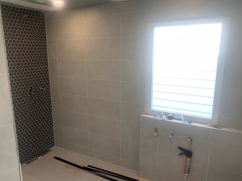 Bathroom with gray tiled walls, shower with dark mosaic tile accent, and a window.