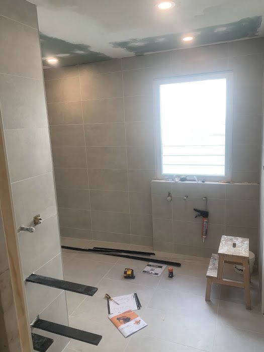 Bathroom under construction with gray tiles, window, tools, and a step stool.