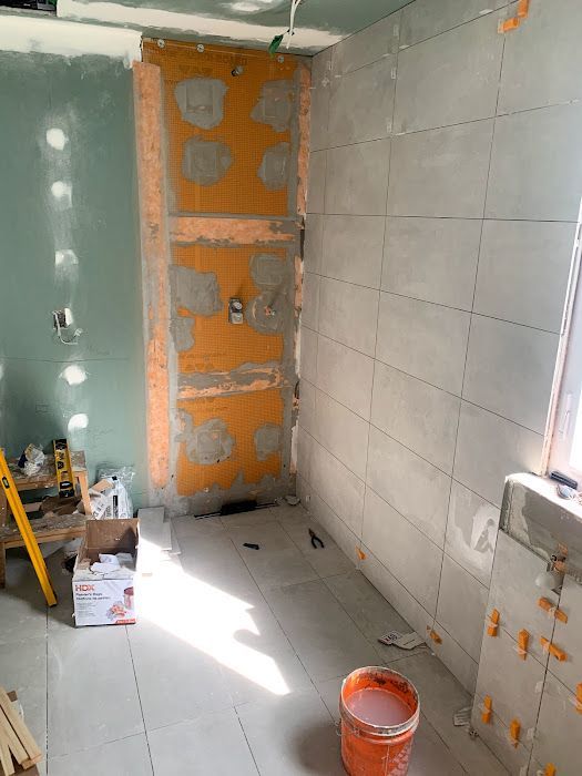 Bathroom under construction; walls with gray tiles and orange waterproofing, tools and materials scattered.