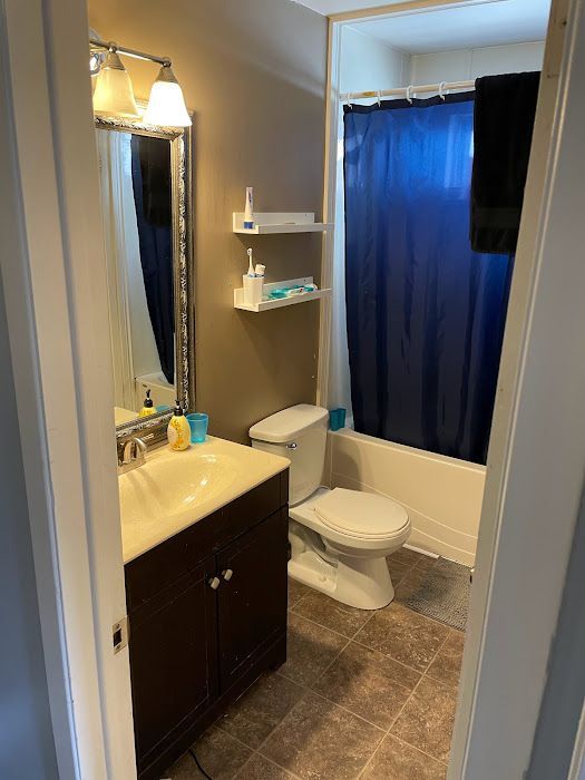Small bathroom with a toilet, sink, and tub, brown and white walls, blue shower curtain.