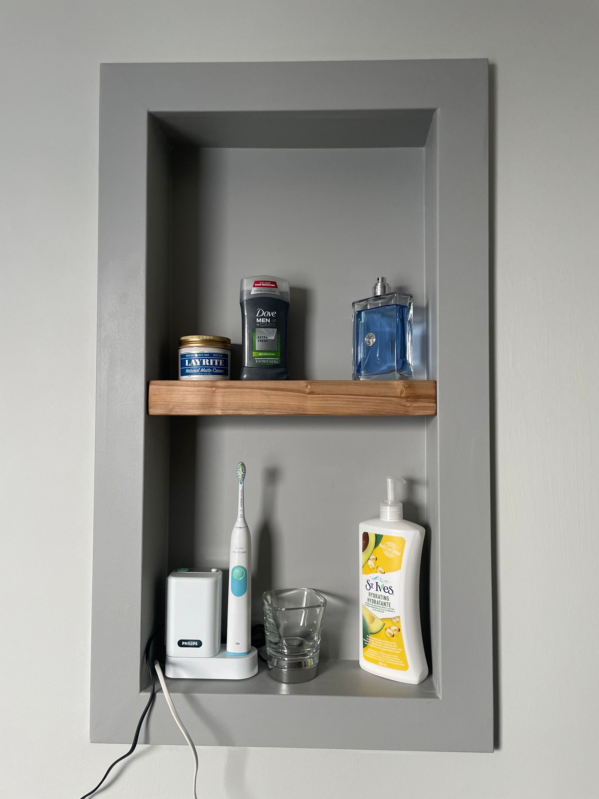 Gray recessed bathroom shelf with toiletries.