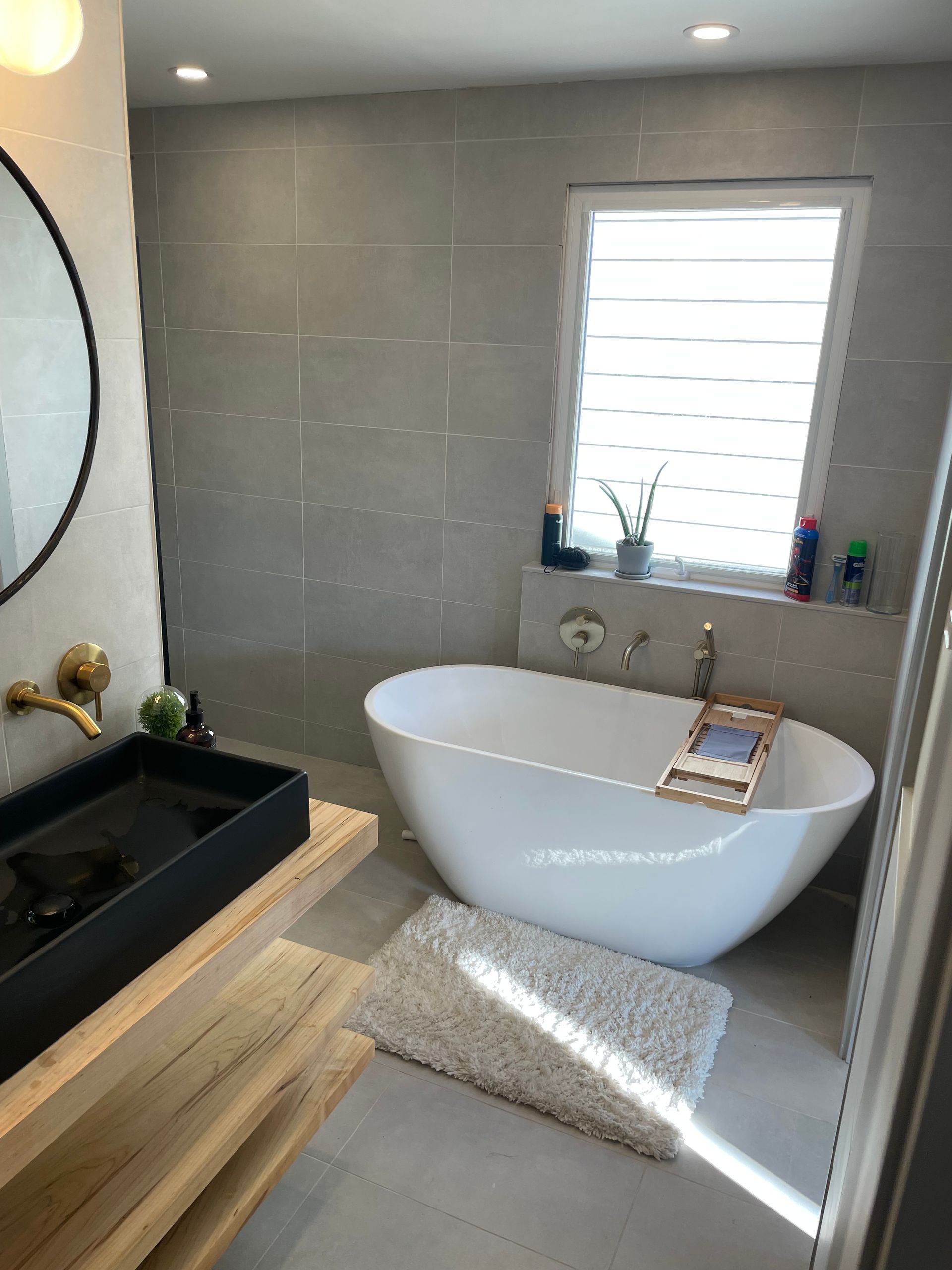 Modern bathroom with a white oval tub, black sink, and gray tiled walls.