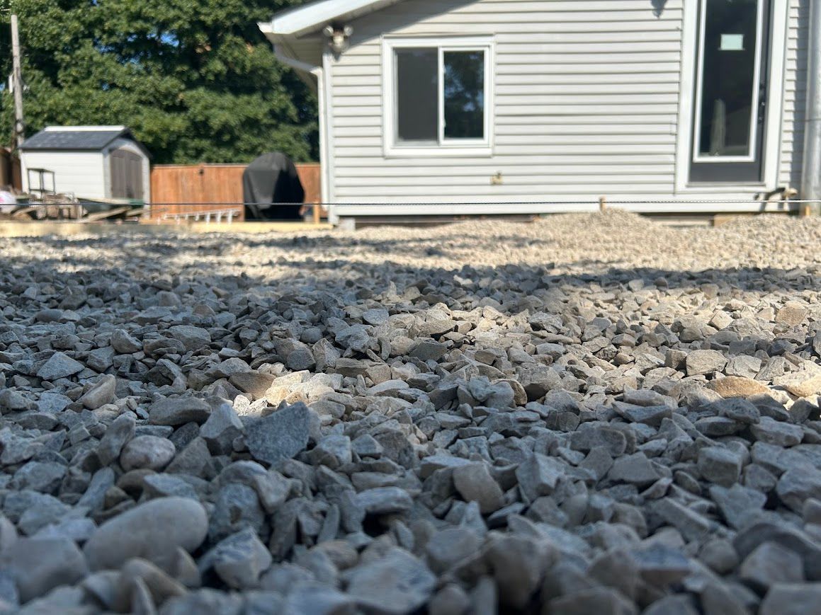 Gravel ground in front of a light-colored house with a window and a door, sunny day.