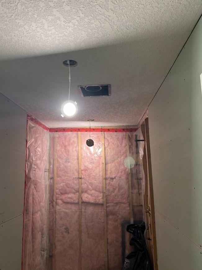 Room under construction, pink insulation on walls, exposed wood framing, light fixture.