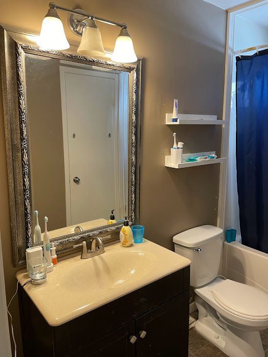 Bathroom with brown walls, vanity, mirror, toilet, and shelves with toiletries; blue shower curtain.