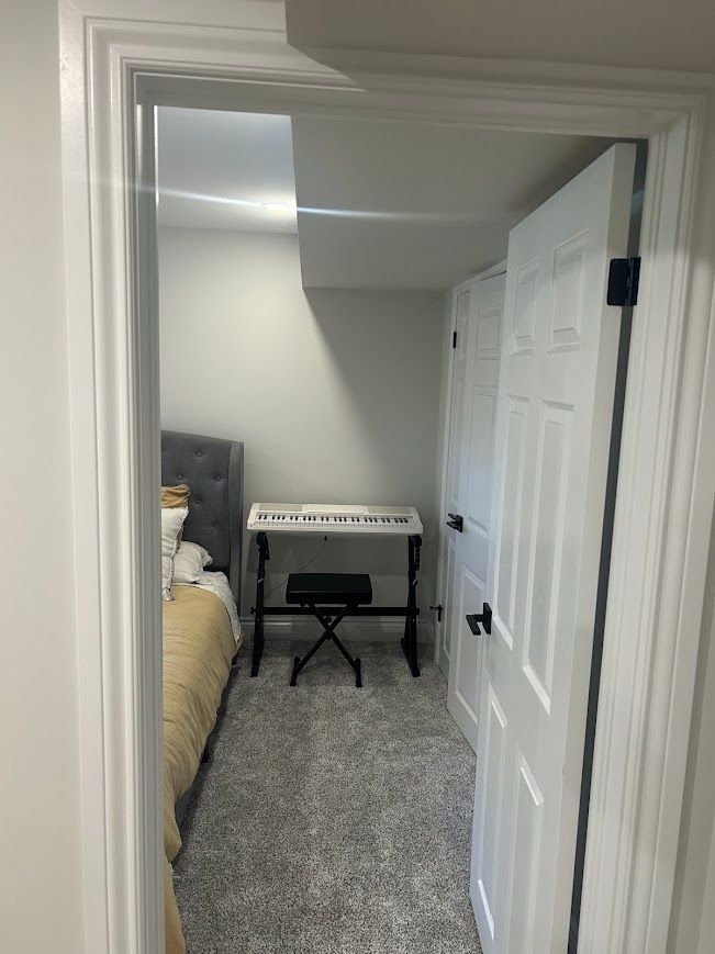 View through a doorway into a room with a bed, keyboard, and two white doors with black hardware.
