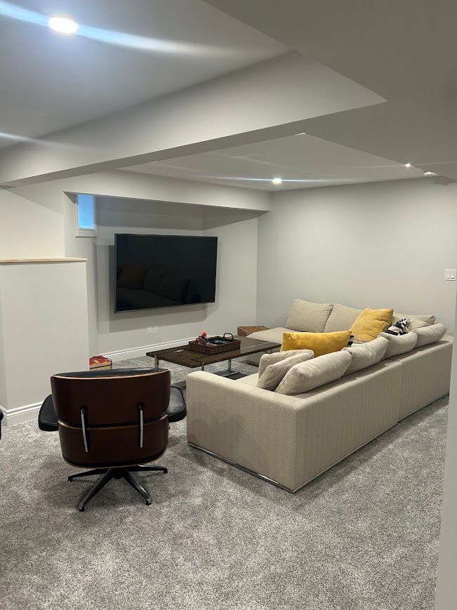 Living room with beige sectional sofa, mounted TV, and brown swivel chair. Gray carpet and walls.