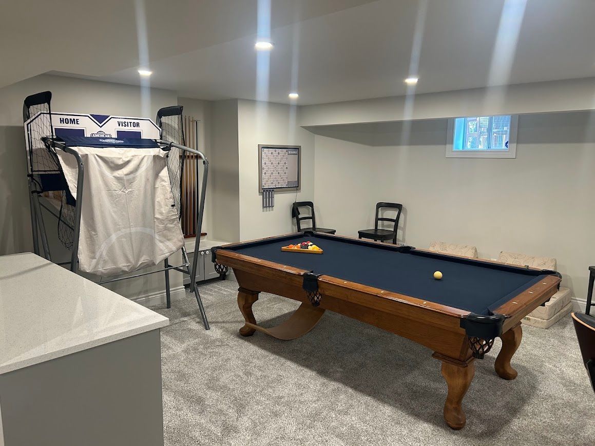 Pool table in a basement game room with a gray rug and light-colored walls.