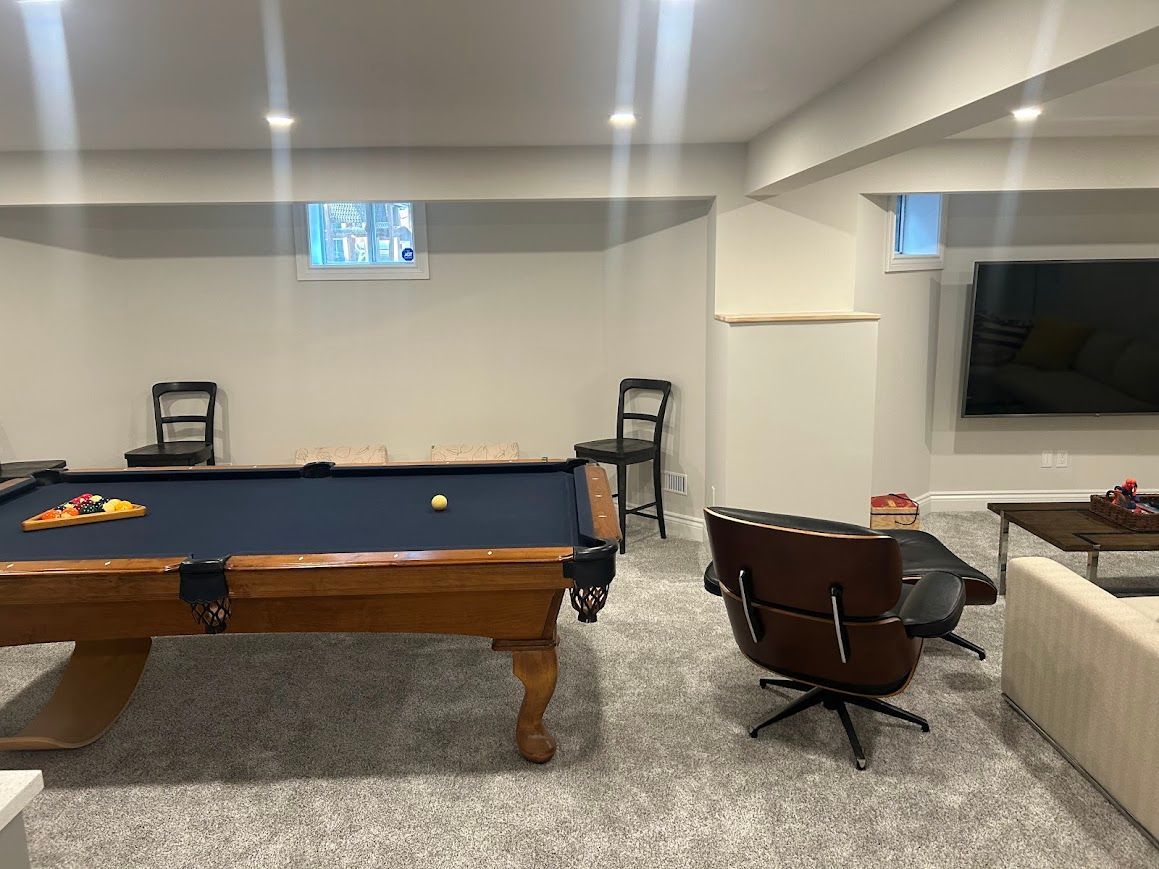 Basement with pool table, chairs, TV, and lounge chair. Light walls, gray carpet, and recessed lighting.