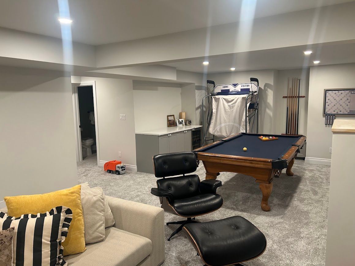 Basement with a pool table, Eames chair, couch with pillows, and a small toy.