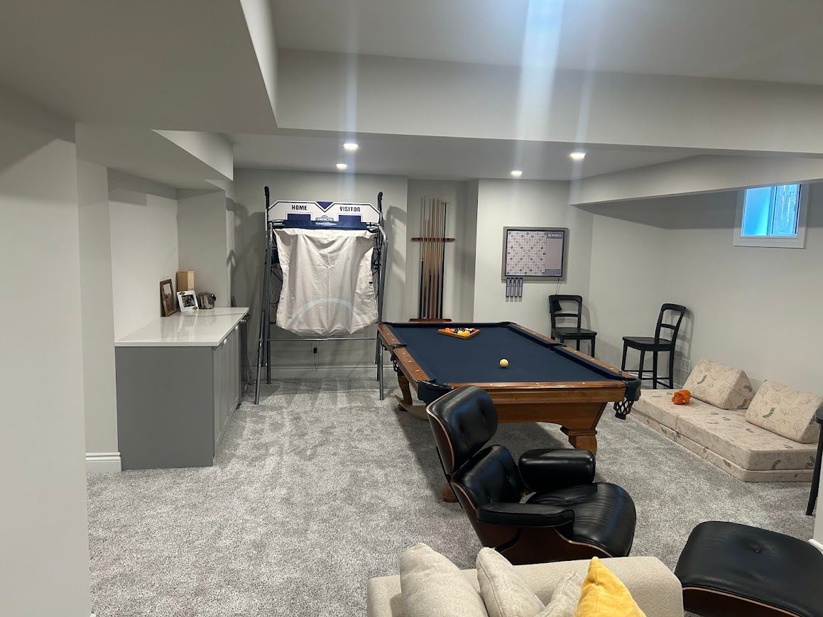 Basement recreation room with pool table, bar, and seating; neutral tones.