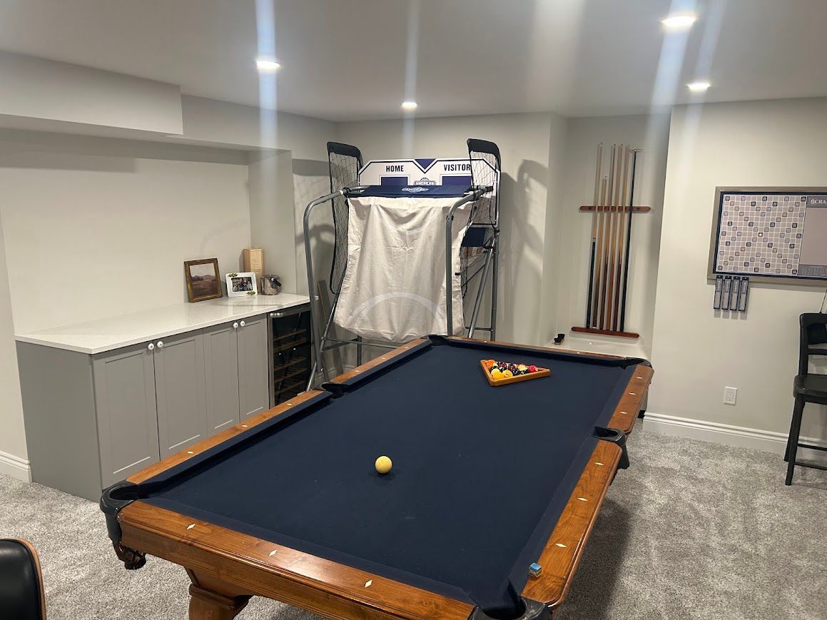 Pool table in a game room with a rack of balls, a gym machine, and a counter.