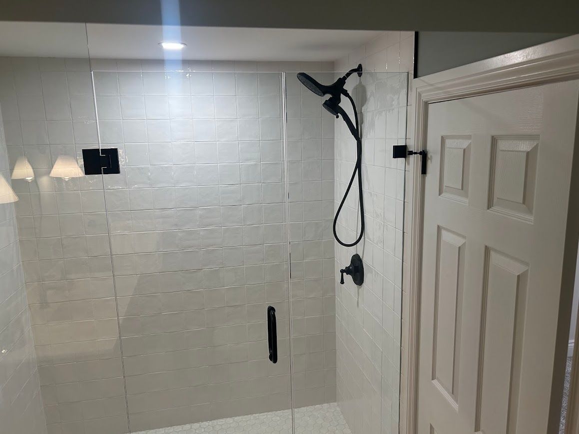 Modern white-tiled shower with glass door and black fixtures. Adjacent white door with ornate trim.