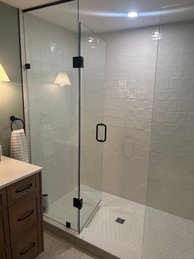 Glass shower enclosure with black hardware, white tile walls, and vanity with wooden cabinets.